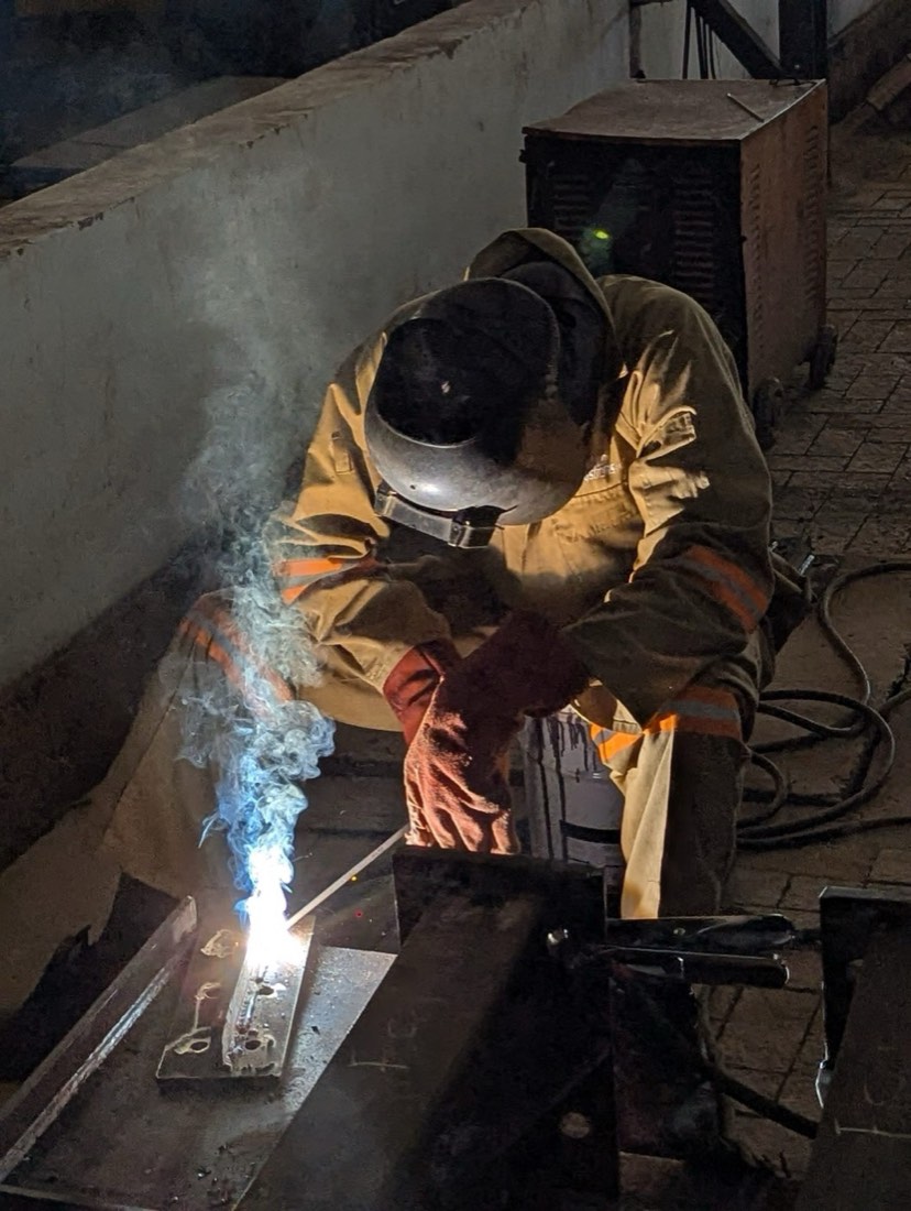 Welder in a helmet running a bead, with sparks and smoke rising from the joint